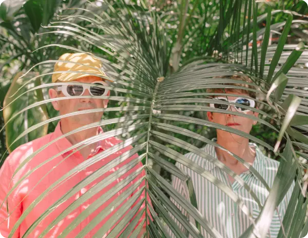 two people behind a palm tree in sun glasses
